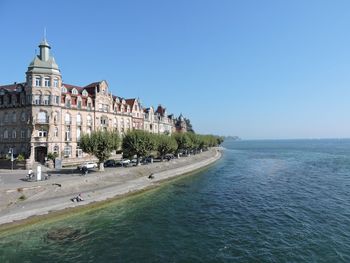 Buildings by sea against blue sky