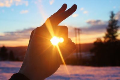 Sun streaming through hand sign on snowy field against sky during sunset