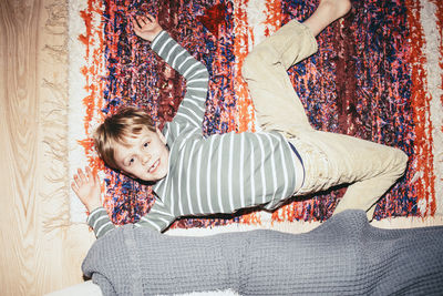 Directly above portrait of smiling boy lying down on rug at home