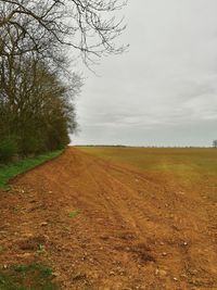 Dirt road amidst field against sky