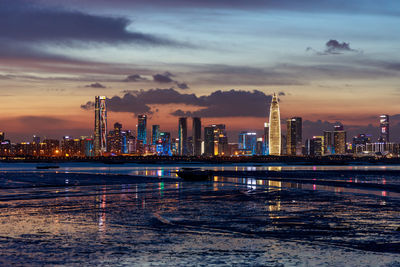 Illuminated buildings in city against sky during sunset