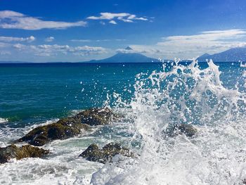 Water splashing on rocks by sea against sky