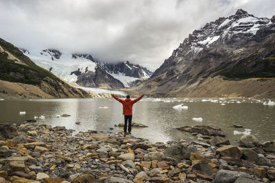 Rear view of person standing on rock by lake against sky