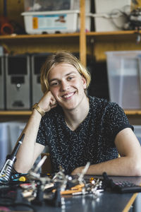 Portrait of smiling young male student sitting with science project at desk in classroom at high school