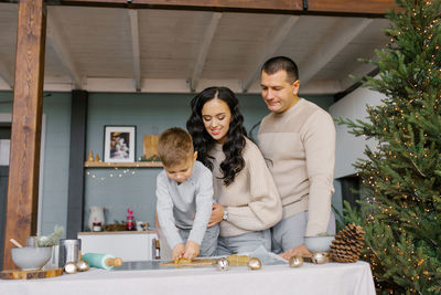 Mom, dad and little son cut out shapes from dough for ginger cookies or gingerbread house.