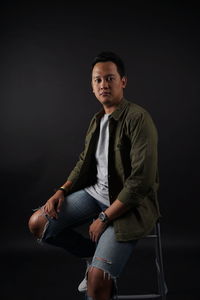 Portrait of young man sitting against black background