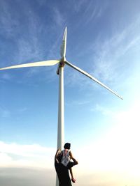 Father showing windmill to daughter against sky