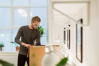 Young businessman opening cardboard box at illuminated creative office