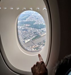 Cropped hand of woman pointing towards airplane window