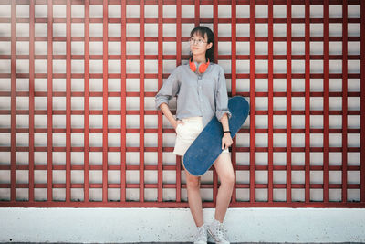 Full length of young woman with skateboard against patterned wall