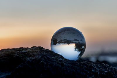 Close-up of crystal ball on rock against sky during sunset