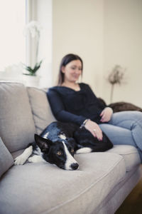 Woman sitting with dog on sofa at home