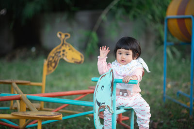 Cute girl waving while sitting on equipment in playground