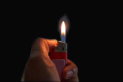 Close-up of hand holding candle against black background