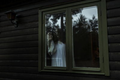 Female ghost looking through glass window of haunted cabin