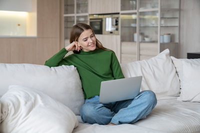 Happy woman watching movie, series or video on laptop sitting on couch at home.