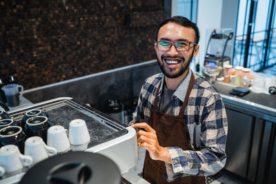 Happy barista standing by coffee machine in cafe