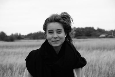 Portrait of smiling young woman standing on field against sky