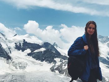 Young woman standing on snowcapped mountain against sky