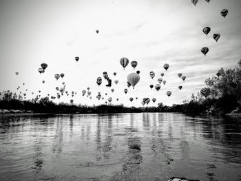 Flock of hot air balloons flying over lake against sky