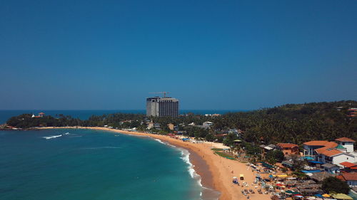 Scenic view of sea by buildings against clear blue sky