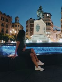 Woman sitting by swimming pool in building against sky