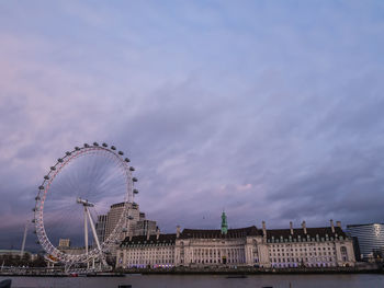 Ferris wheel in city against cloudy sky