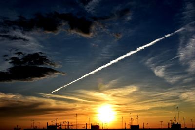 High section of silhouette buildings against vapor trail in sky at sunset