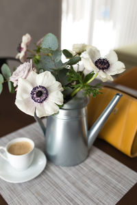 Delicate anemones flowers in a metal pot vase with a cup of coffee on the wooden table, hand bag