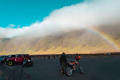 People riding bicycles on road against rainbow in sky