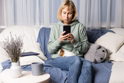 Portrait of young woman using mobile phone while sitting on sofa at home