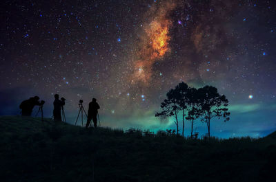 Silhouette men photographing while standing on land against sky at night