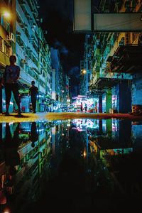 People on illuminated street by buildings in city at night