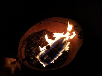 Close-up of hand holding illuminated candle against black background