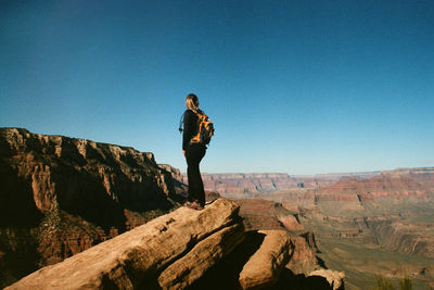 Low angle view of woman standing on rock against clear blue sky