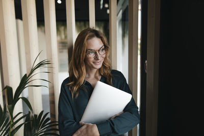 Smiling businesswoman holding laptop looking sideways