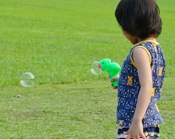 Boy playing with bubbles while standing on field