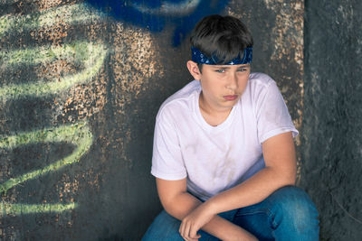 Portrait of young man sitting against wall