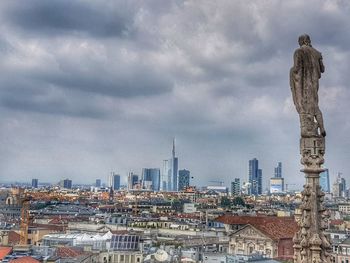 Statue of buildings in city against cloudy sky