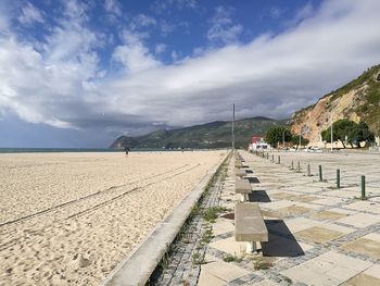 Empty benches on promenade at beach against sky