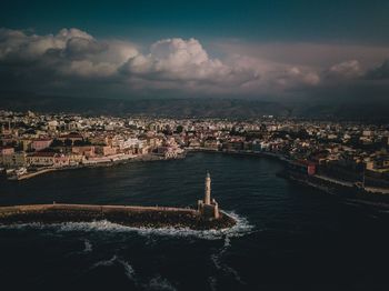 Aerial view of cityscape by sea against cloudy sky during sunset