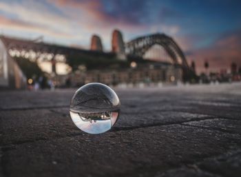 Close-up of crystal ball by water against sky in city