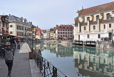 People on canal amidst buildings in city against sky