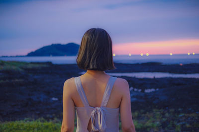 Rear view of woman looking at sea against sky during sunset