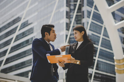 Low angle view of colleagues discussing file while standing against building in city