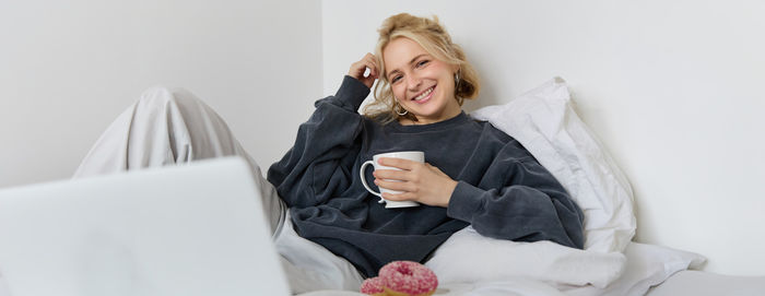 Portrait of young woman using digital tablet while sitting on bed at home