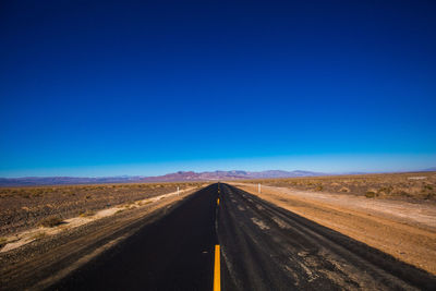 Road passing through land against clear blue sky