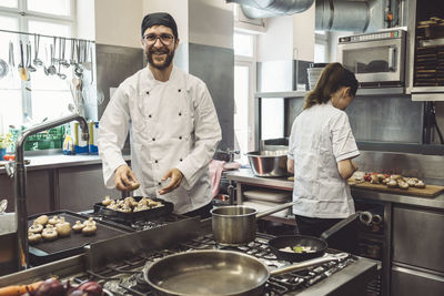 Portrait of smiling male chef cooking mushrooms in commercial kitchen