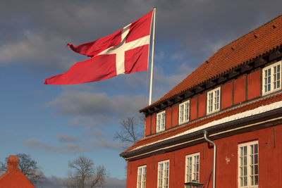 Low angle view of red flag on roof against sky