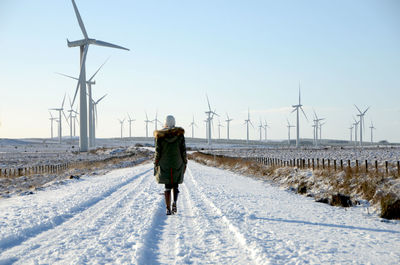 Woman walking on snow covered road against wind turbines